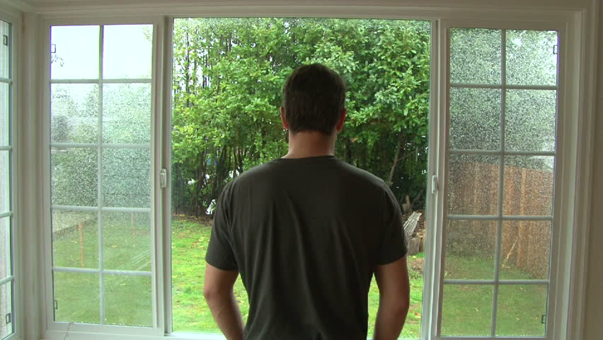 Man Looking Out Window Watching Heavy Wind And Rain During Storm Stock