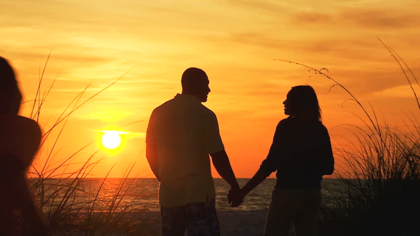 Young Family In Silhouette Standing On Beach Holding Hands Watching