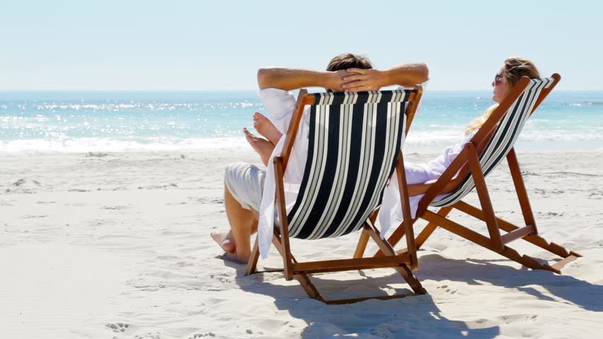 An Elderly Couple Sits On The Beach Together And Holds Hands. Stock ...