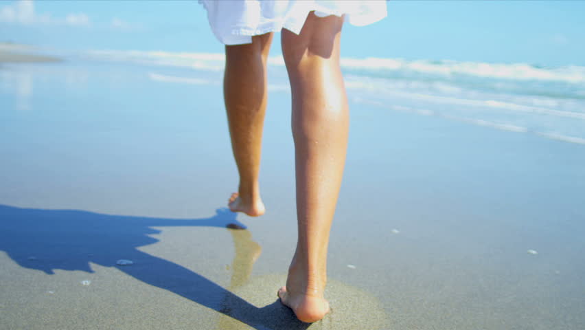 Bare legs feet young African American girl walking on wet sand beside ...