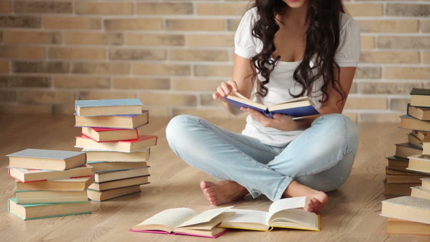 Charming Girl Sitting On Floor With Stack Of Books Reading One And ...